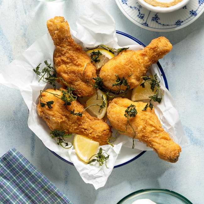 Αλατοπιπερώστε τα κοπανάκια κοτόπουλου και αφήστε τα στην άκρη. Σε ένα πιάτο βάλτε το αλεύρι, σε ένα μπολάκι σπάστε τα αυγά προσθέτοντας λίγο αλάτι και πιπέρι και σε ένα άλλο πιάτο βάλτε τη φρυγανιά. Πανάρετε τα κοπανάκια, ξεκινώντας από το αλεύρι, έπειτα στο αυγό και τέλος στη φρυγανιά. Τηγανίστε τα παναρισμένα κοπανάκια σε καυτό ηλιέλαιο για περίπου 20-25 λεπτά μέχρι να ροδίσουν. Αποσύρετε σε ένα πιάτο με απορροφητικό χαρτί. Στο ίδιο τηγάνι τηγανίστε και τα φύλλα του μαϊντανού. Σε ένα blender τοποθετήστε την Alpiland φρέσκια Mozzarella, προσθέστε την επιθυμητή ποσότητα σάλτσα Sriracha chili, το σησαμέλαιο και πολτοποιήστε το μίγμα. Σερβίρετε σε ένα πιάτο 2 κομμάτια κοτόπουλου, λίγο μαϊντανό τηγανισμένο και ένα μπολάκι με τη σάλτσα. Απολαύστε το Steirisches Backhendl!